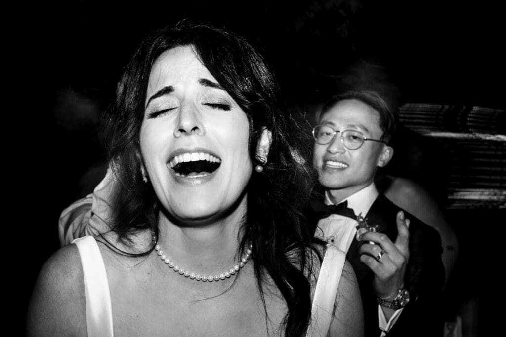 Black and white photo of bride singing close to the camera and groom laughing at Vine Hill House wedding