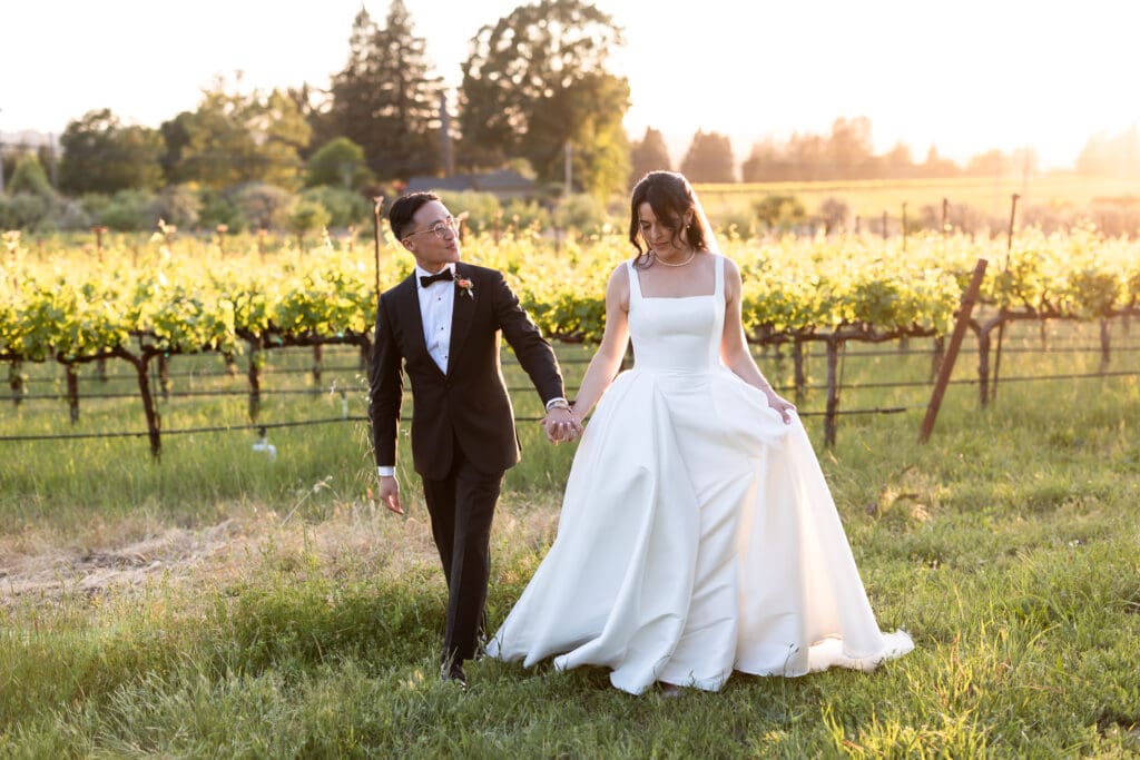 Sunset photo of bride and groom holding hands and walking together in vineyard at Vine Hill House wedding