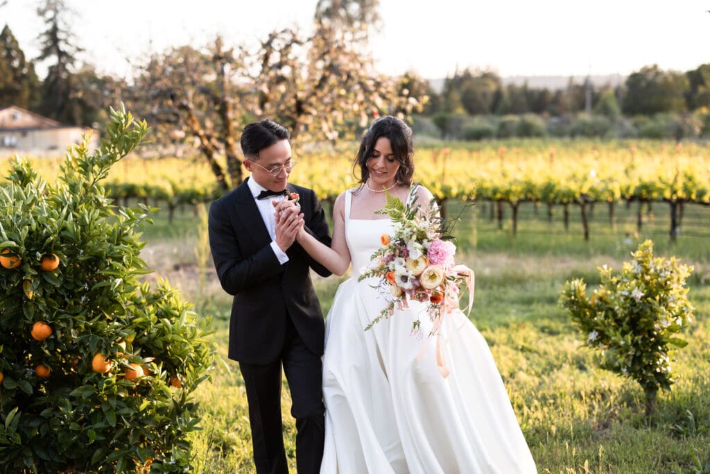 Bride and groom holding hands while bride holds bouquet of flowers at sunset wine country wedding