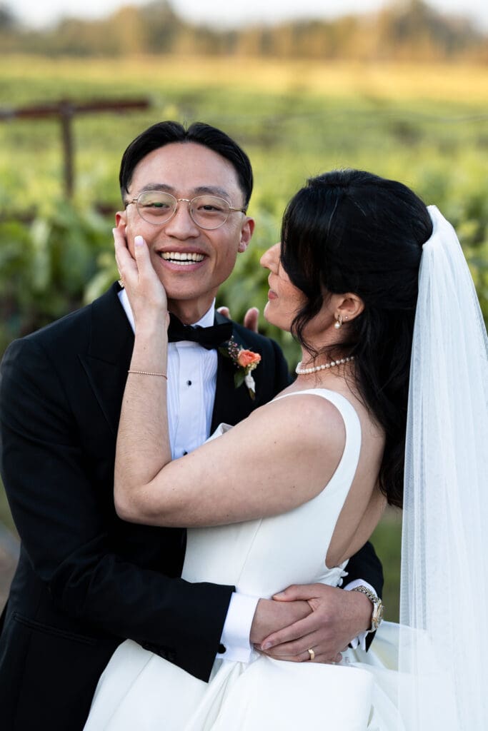 Bride touching groom's face while he is smiling at vineyard wedding in Sonoma County