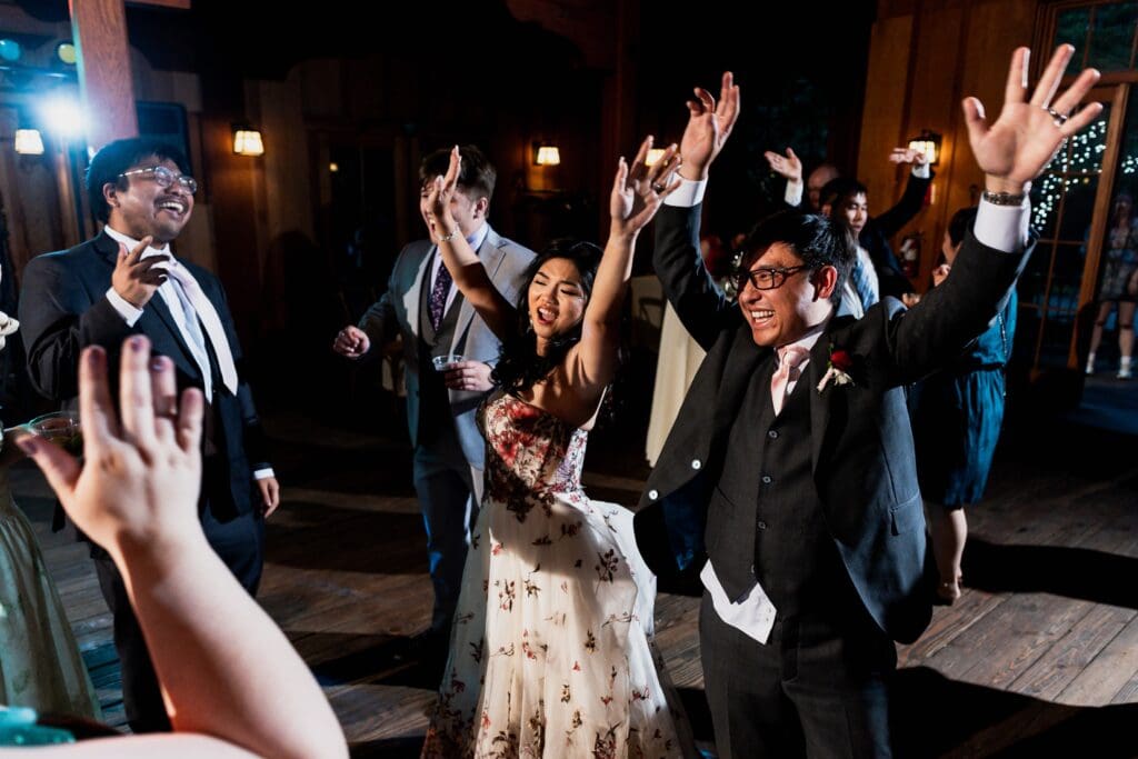 Bride and groom and wedding party dancing with hands up at wedding reception