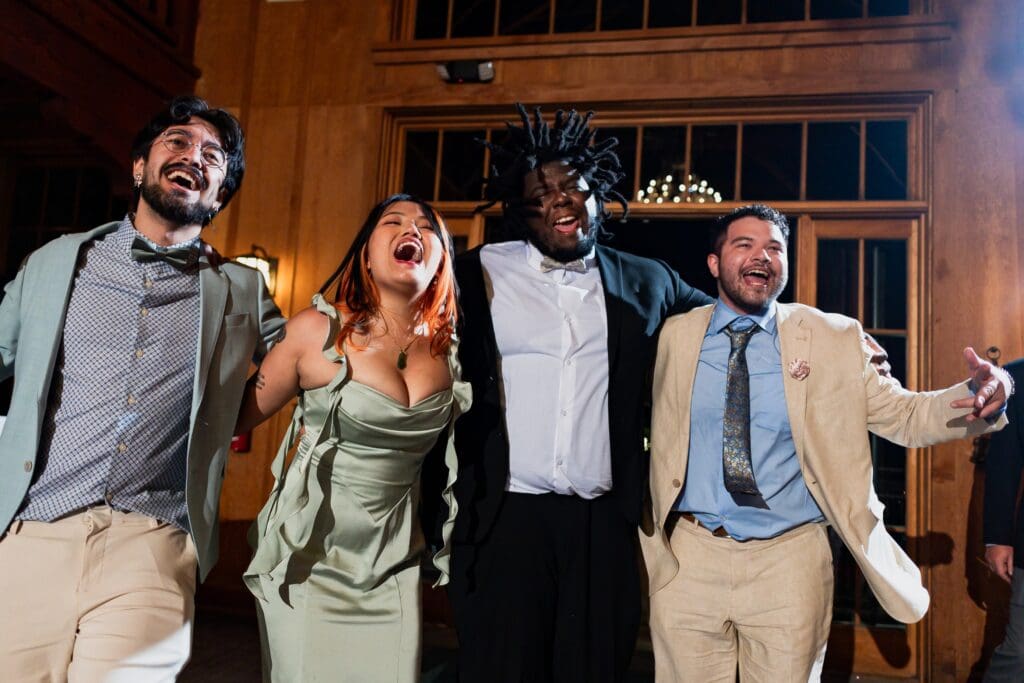 Four wedding guests arm-in-arm and singing at the wedding reception