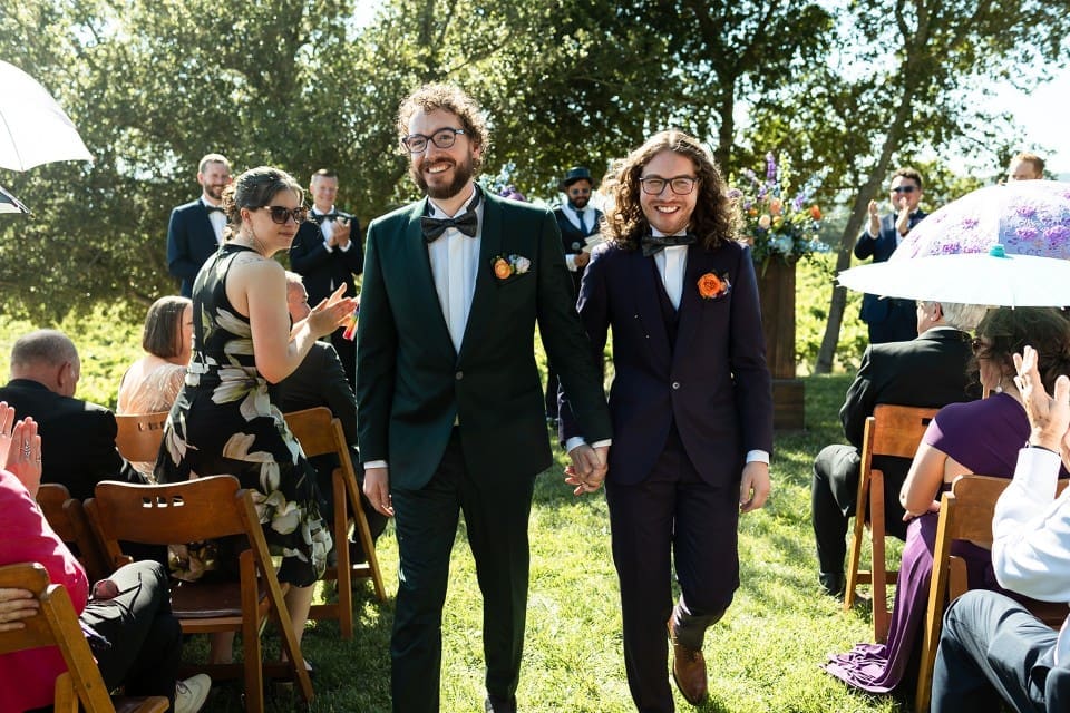 Grooms holding hands walking down the aisle at outdoor wedding in Northern California
