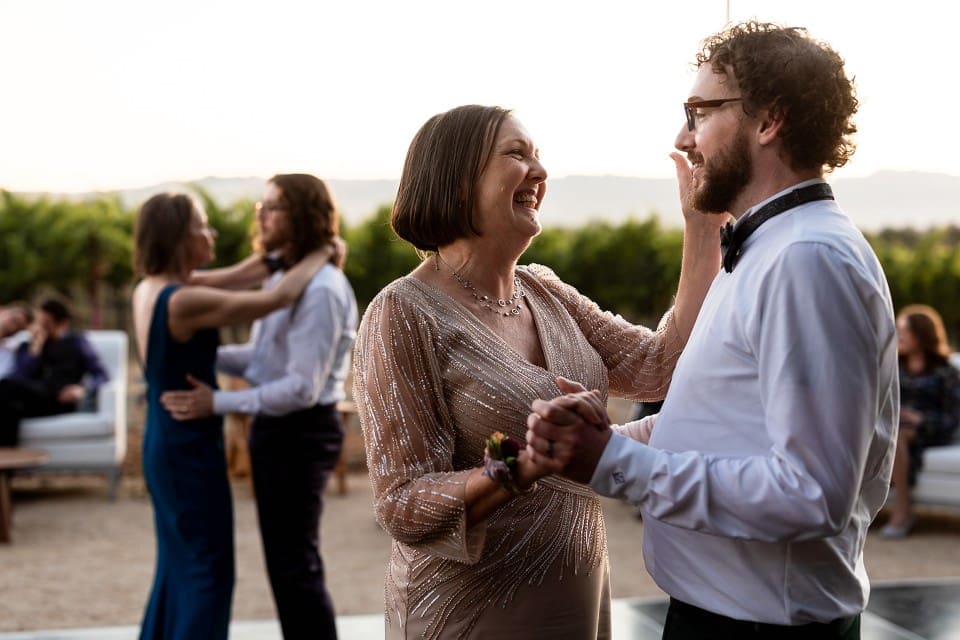 Mother of the groom wiping a tear from his eye during wedding reception