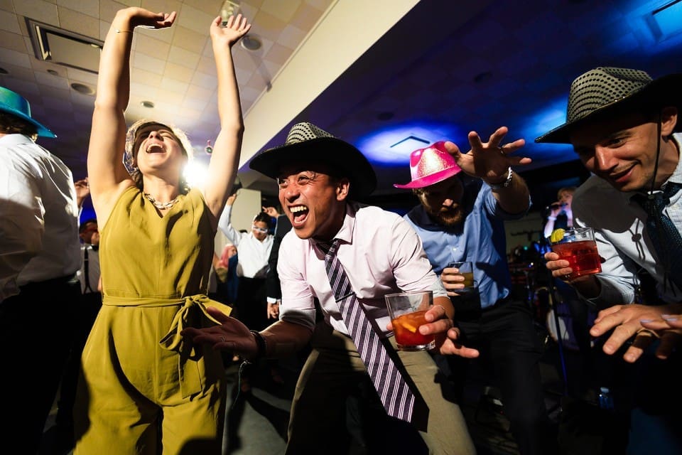 Wedding guests with hats on laughing and dancing at wedding reception