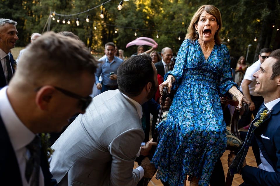 Wedding guest being hoisted up in a chair on the dance floor with a big laugh