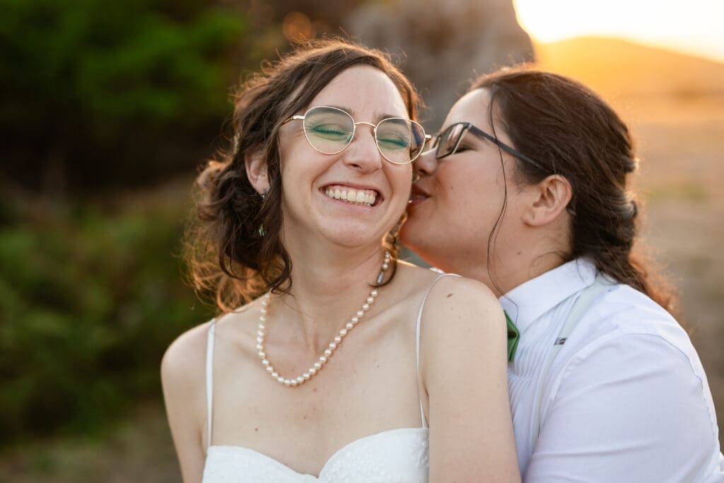 Bride kissing other bride's cheek at Holly’s Ocean Meadow in Fort Bragg, CA