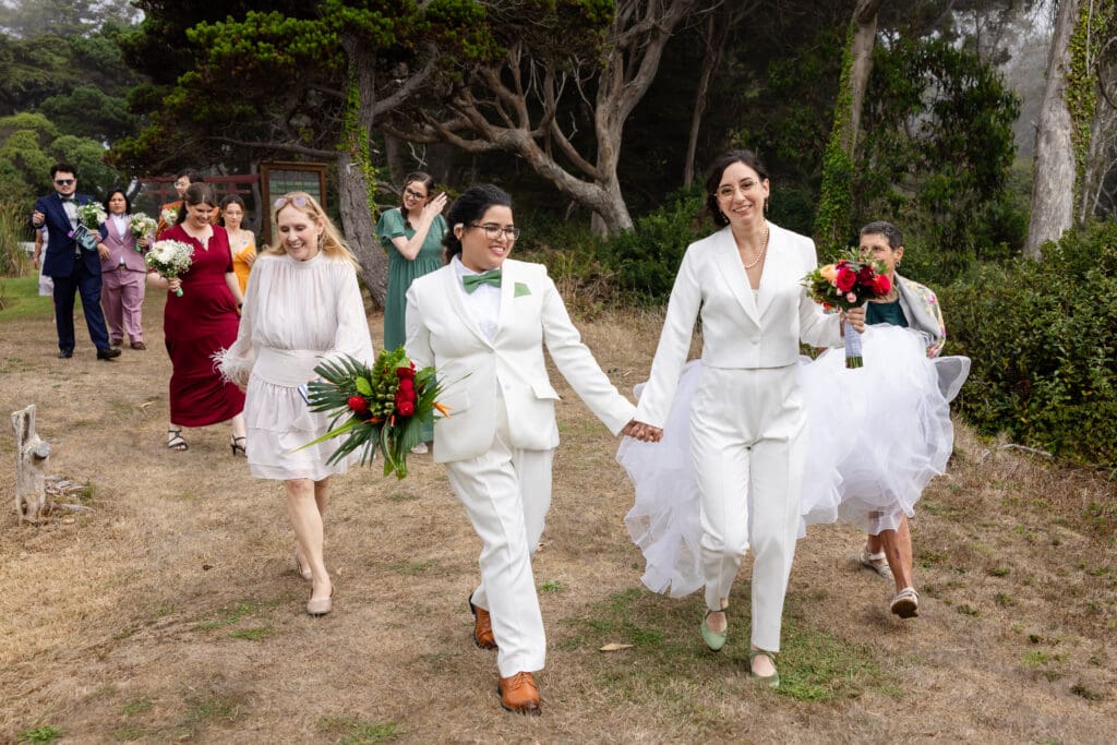 Brides walking down the aisle with rainbow wedding party at Fort Bragg wedding