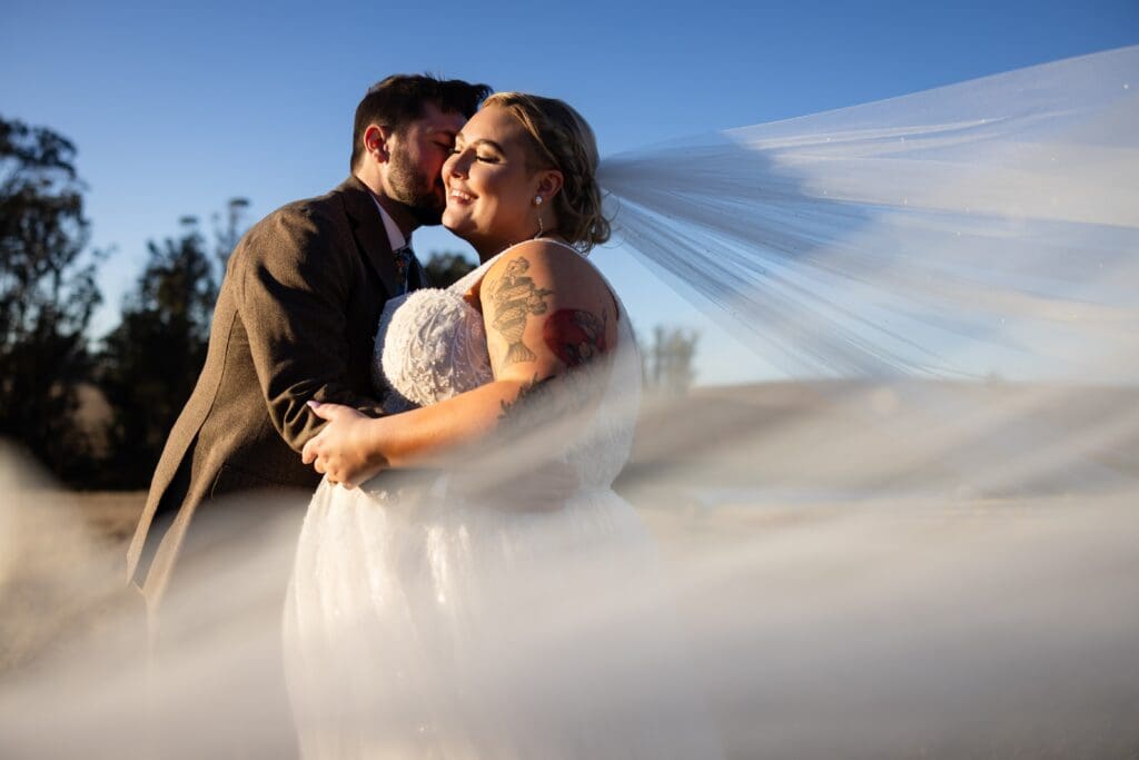 Bride and groom kissing with veil blowing in California wind
