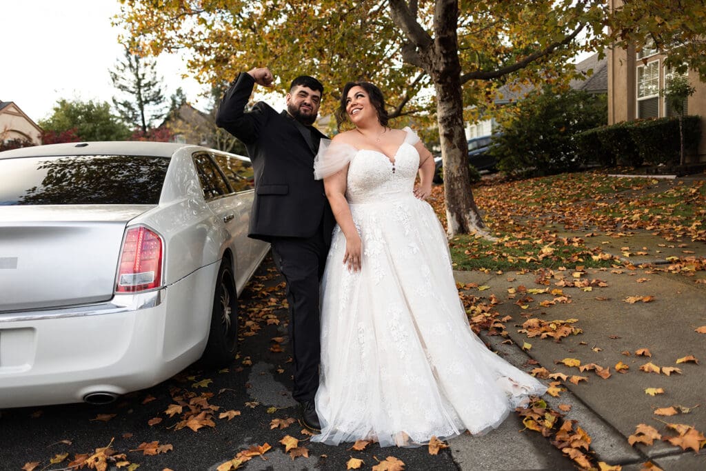 Bride an groom pose with limo before their wedding in a fun moment.
