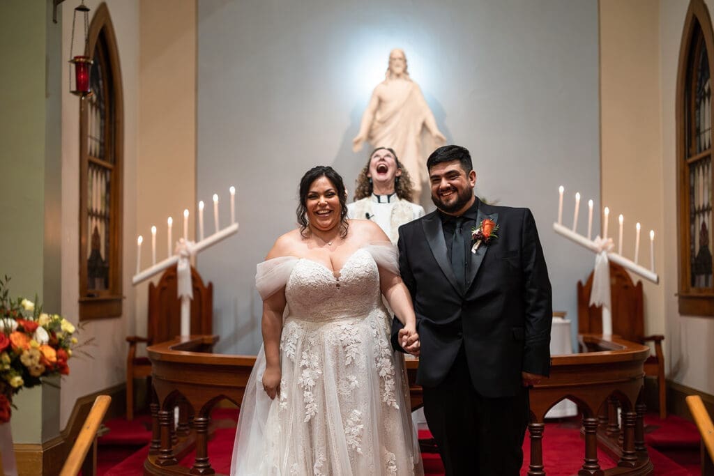 Bride and groom exist their wedding ceremony at Elim Church, Petaluma while priest is caught making a funny face in the background.