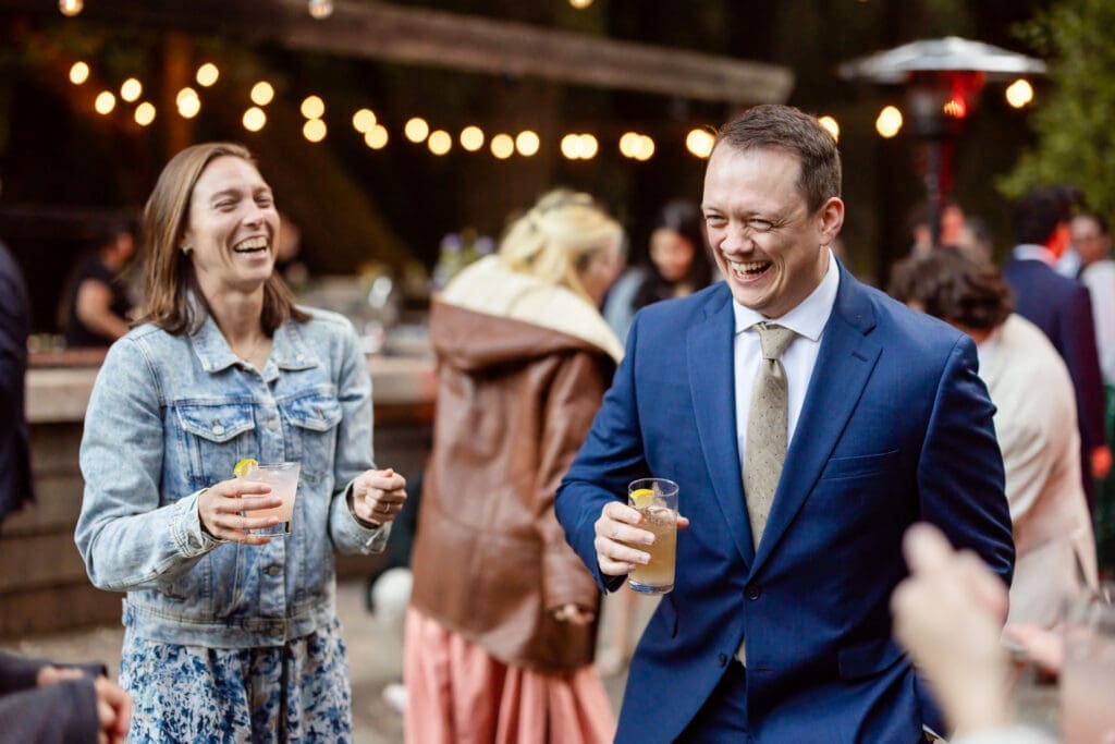 Wedding guests laughing under string lights at a Leonard Lake Reserve summer camp wedding